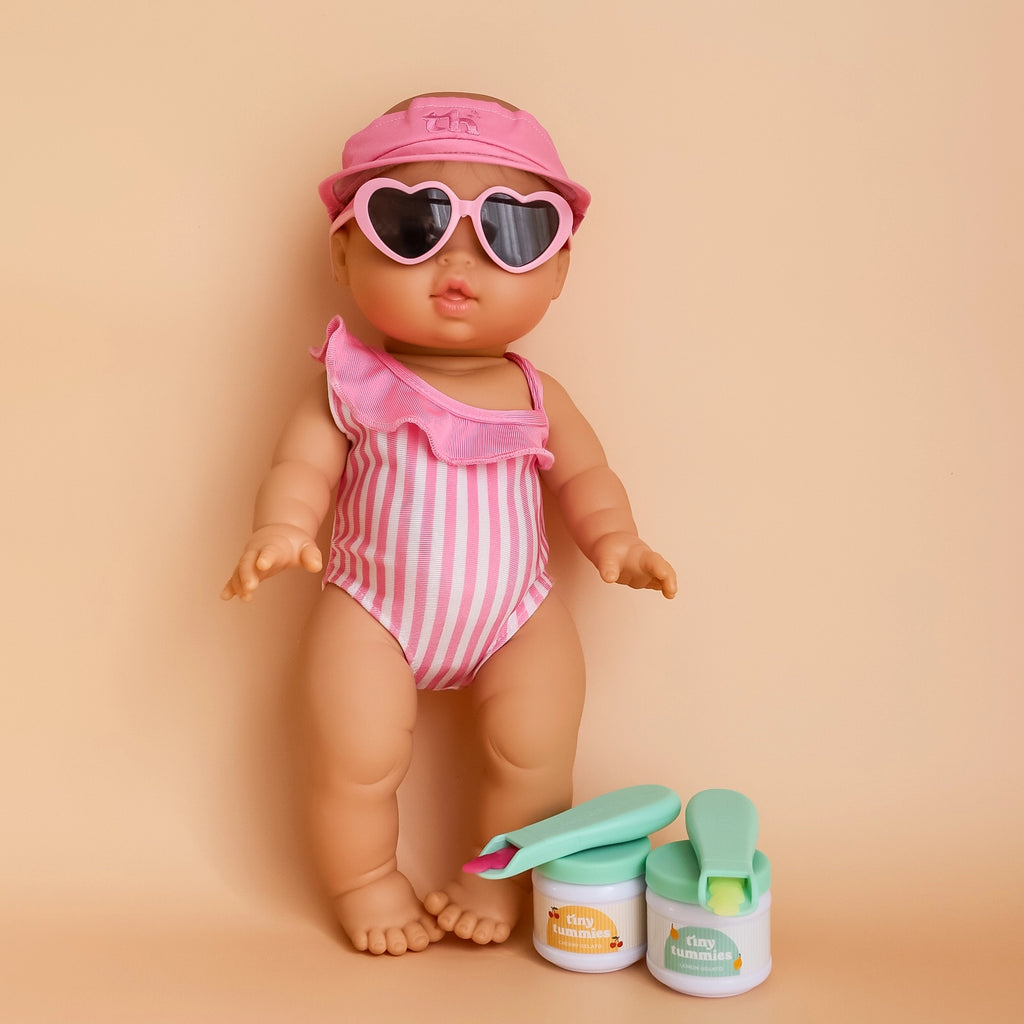 Doll in pink swimmers and pink sunnies and hat with "TH- Tiny Tummies Around the world collection - gelato pack