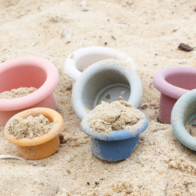 Child stacking Montessori style silicone stacking cups from Cherub Baby close up at beach with sand in them