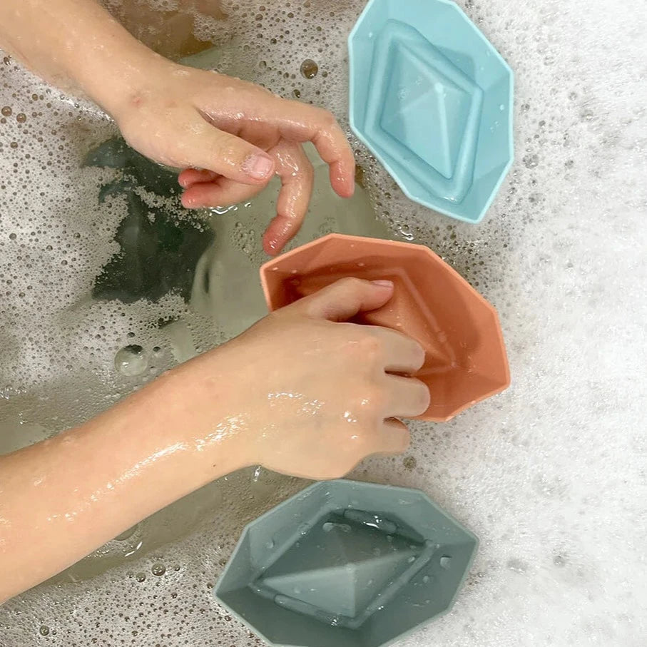 Child playing with blue, orange and grey silicone bath toy ships in bath with bubbles