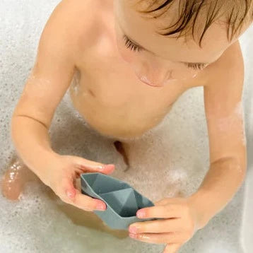 Child playing with grey silicone bath toy ships in bath with bubbles