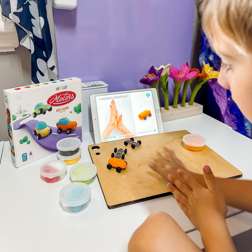 Child sitting and making hey clay eco cars on wooden playmat 