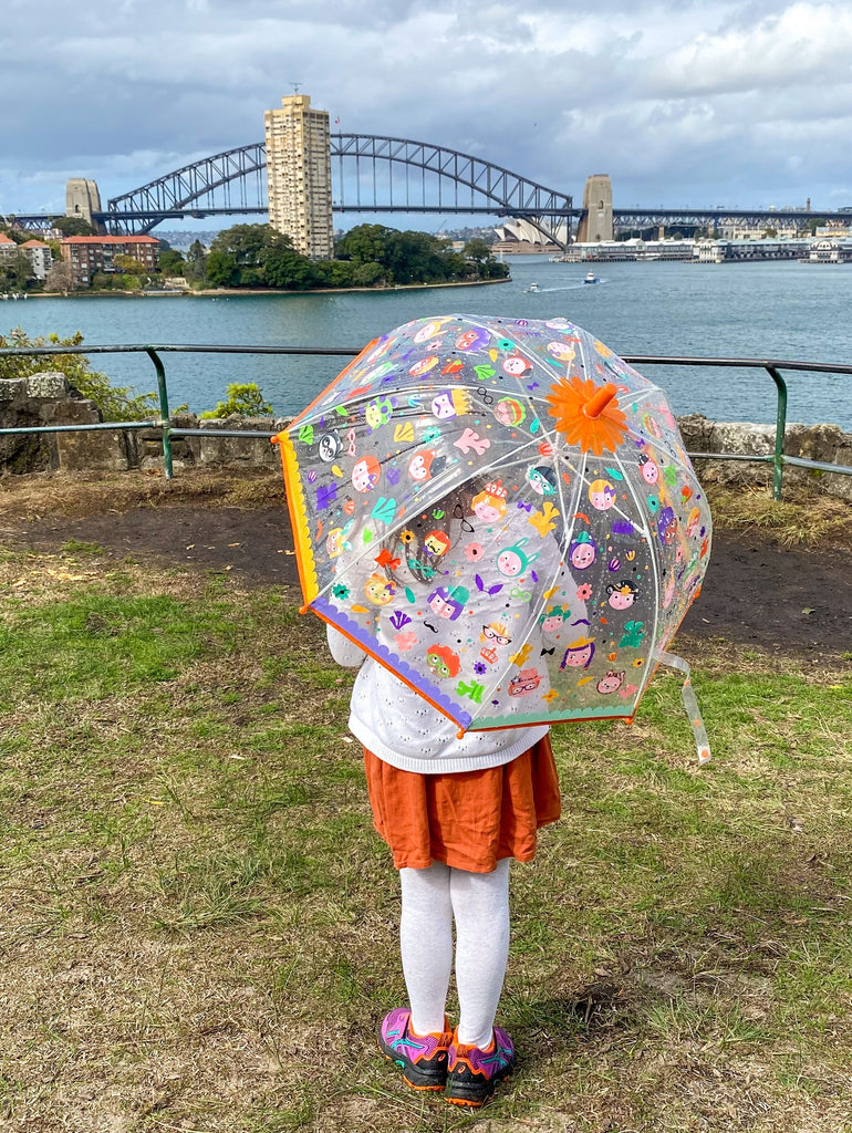 Djeco colour changing umbrella held by child looking across sydney harbour at the harbour bridge on a cloudy day