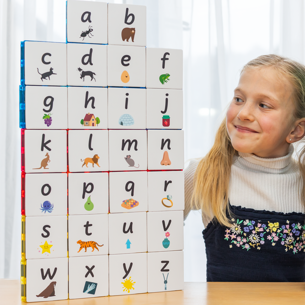 Girl smiling at magnetic tiles with lowercase alphabet toppers on them