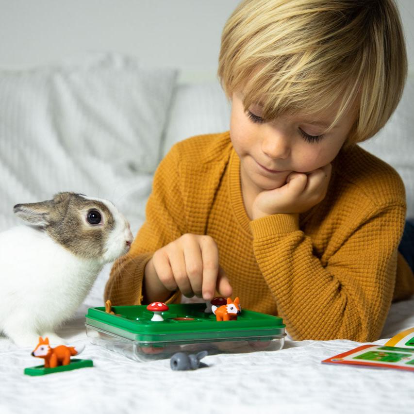 Child playing puzzle game Jump In with pet rabbit sitting on bed next to him