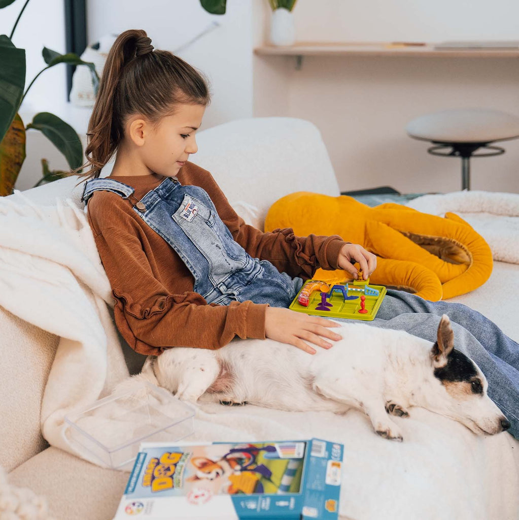 Child playing smart dog game on couch with dog by her side
